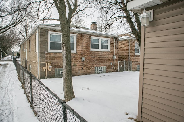 snow covered house featuring brick siding, a chimney, and fence