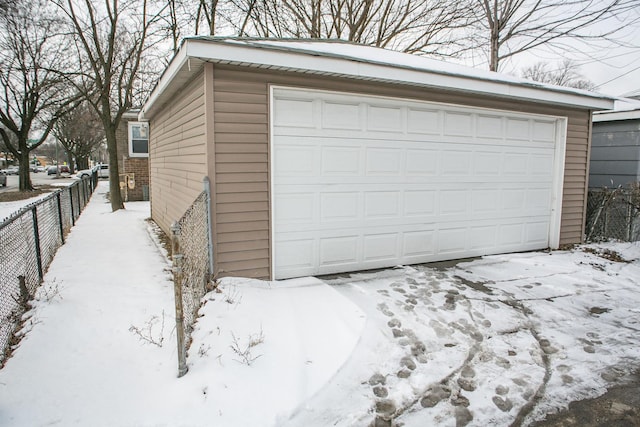 snow covered garage featuring a detached garage and fence