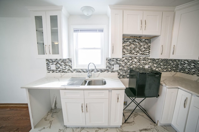 kitchen with decorative backsplash, glass insert cabinets, marble finish floor, white cabinetry, and a sink