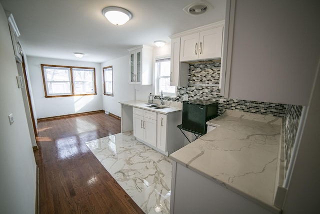 kitchen featuring a sink, visible vents, white cabinetry, tasteful backsplash, and glass insert cabinets