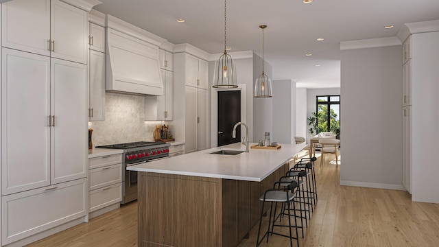 kitchen featuring an island with sink, white cabinetry, premium range hood, sink, and range with two ovens