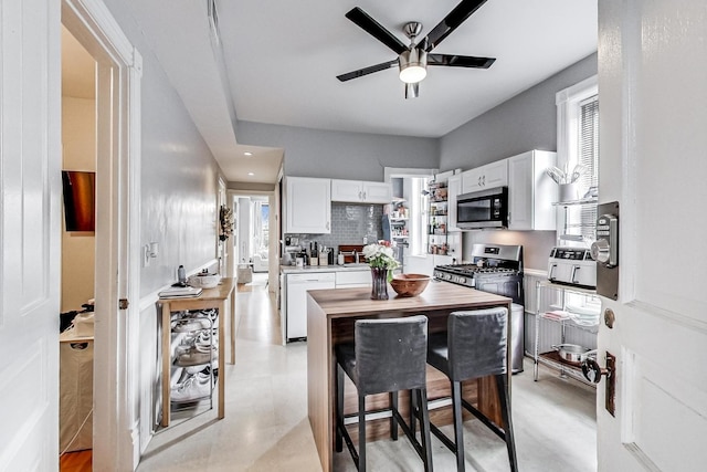 kitchen with white cabinetry, ceiling fan, appliances with stainless steel finishes, a breakfast bar area, and decorative backsplash