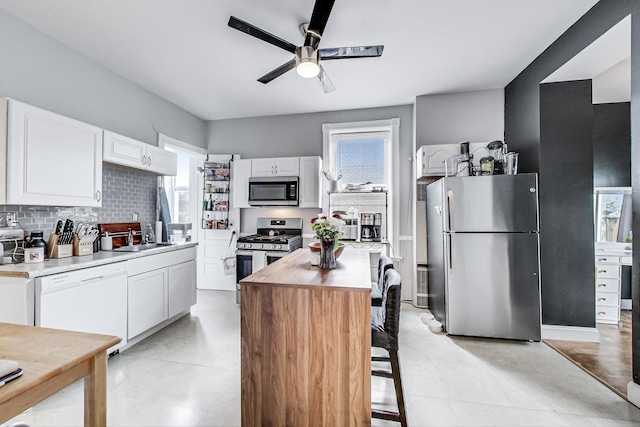 kitchen with stainless steel appliances, white cabinets, decorative backsplash, a center island, and sink