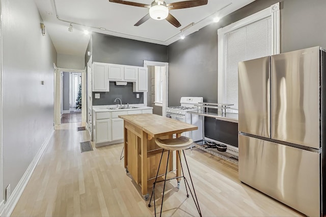 kitchen featuring light hardwood / wood-style flooring, white range with gas stovetop, stainless steel refrigerator, sink, and white cabinetry