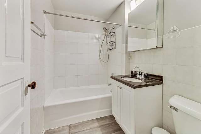 full bathroom with hardwood / wood-style floors, tile walls, vanity, tiled shower / bath combo, and toilet