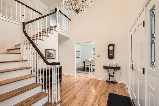 entryway with a notable chandelier, light hardwood / wood-style floors, and a towering ceiling