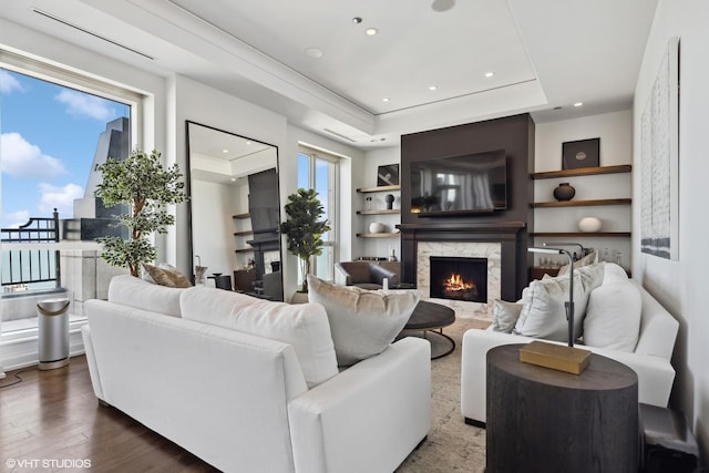 living room featuring a high end fireplace, wood finished floors, a tray ceiling, built in shelves, and recessed lighting