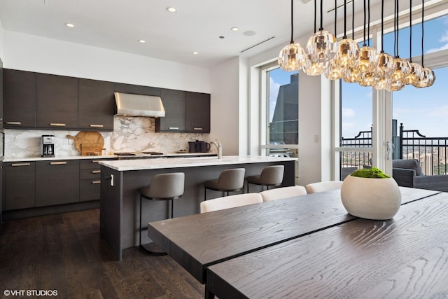 kitchen featuring a breakfast bar area, dark wood-style flooring, light countertops, ventilation hood, and tasteful backsplash