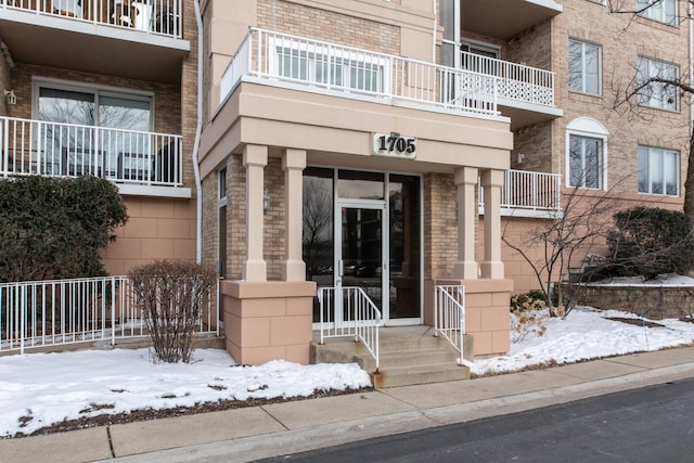 snow covered property entrance featuring brick siding