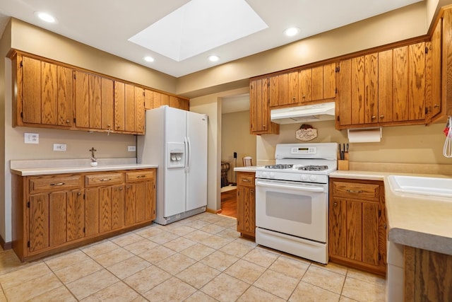 kitchen with white appliances, brown cabinetry, a skylight, and under cabinet range hood