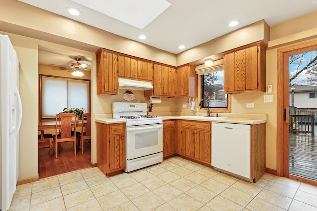 kitchen featuring white appliances, under cabinet range hood, light countertops, and a sink