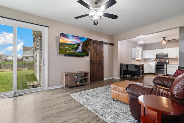 living room with light wood-type flooring, ceiling fan, and a barn door