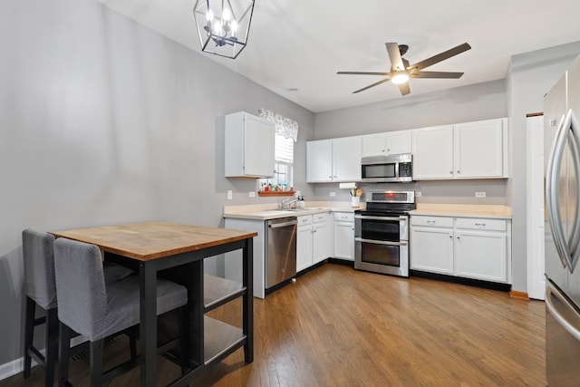 kitchen featuring white cabinetry, sink, dark wood-type flooring, appliances with stainless steel finishes, and ceiling fan with notable chandelier