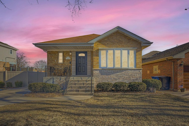 view of front of home featuring fence, a lawn, and stone siding