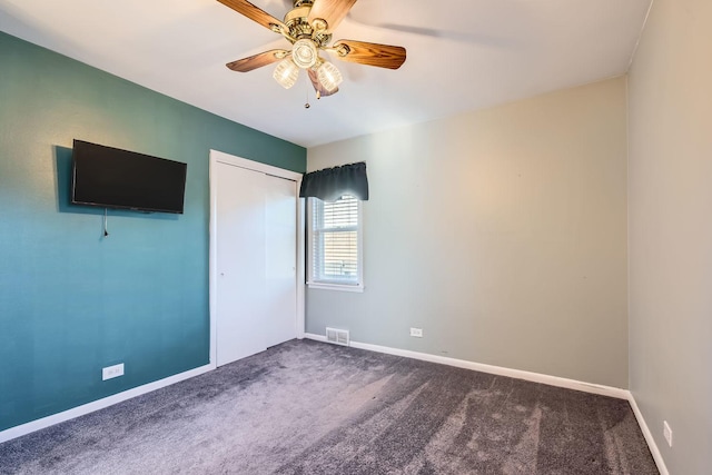 unfurnished bedroom featuring baseboards, dark colored carpet, visible vents, a ceiling fan, and a closet