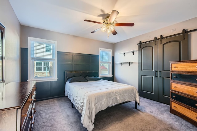 bedroom featuring a decorative wall, a ceiling fan, dark carpet, and a barn door