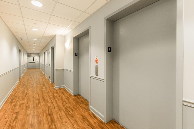 hallway with a drop ceiling, elevator, and hardwood / wood-style floors