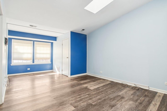 empty room with a skylight, visible vents, and wood finished floors