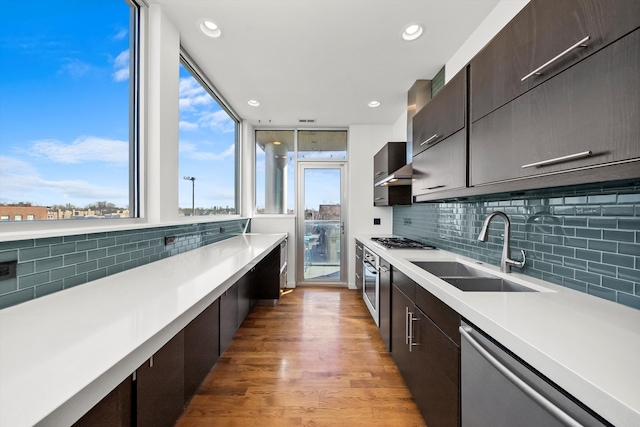 kitchen with light wood-style flooring, a sink, light countertops, dark brown cabinetry, and appliances with stainless steel finishes