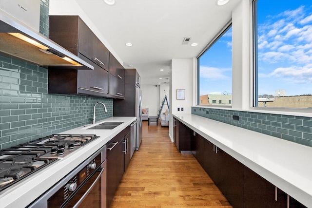 kitchen with visible vents, wall chimney range hood, light countertops, light wood-type flooring, and a sink