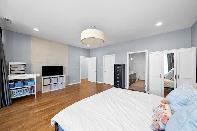 bedroom featuring wood finished floors, visible vents, baseboards, ensuite bath, and recessed lighting