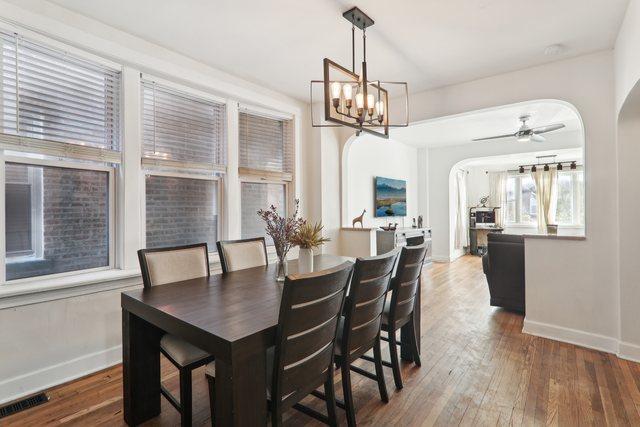 dining space with ceiling fan with notable chandelier and dark hardwood / wood-style flooring