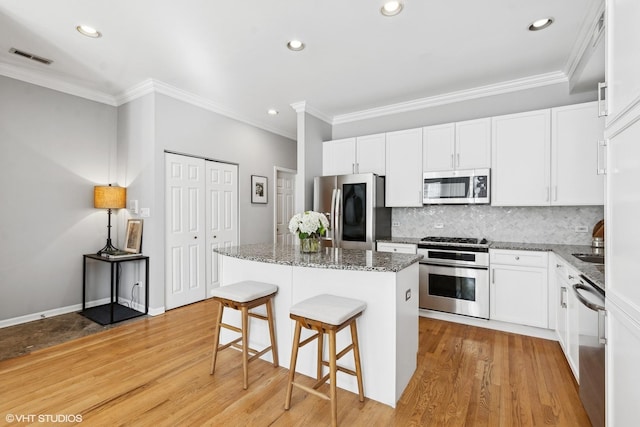 kitchen featuring white cabinets, stainless steel appliances, dark stone counters, and a center island