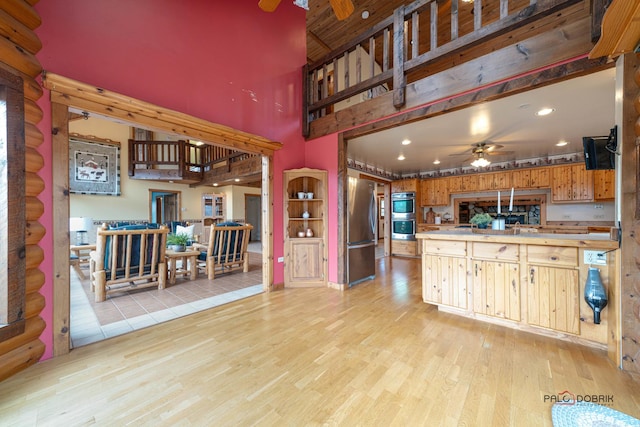 kitchen with log walls, light wood finished floors, appliances with stainless steel finishes, a ceiling fan, and a peninsula