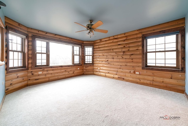 carpeted spare room featuring rustic walls, a wealth of natural light, and a ceiling fan