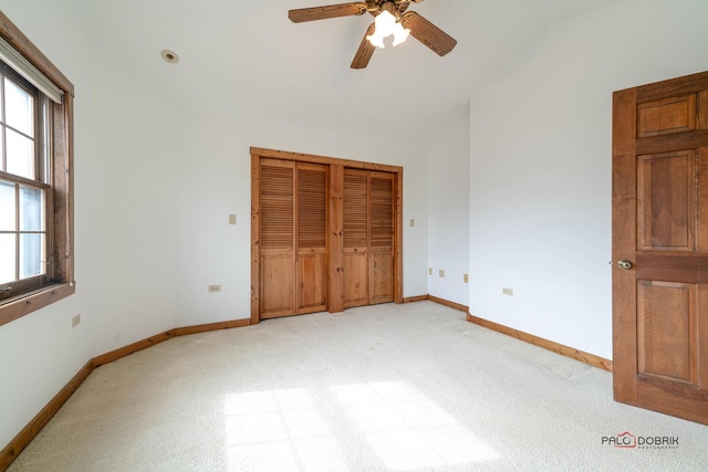 unfurnished bedroom with lofted ceiling, a closet, light carpet, and baseboards