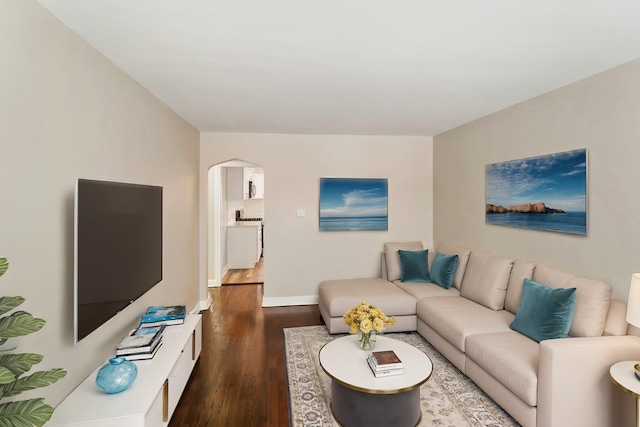 living area featuring dark wood-type flooring, arched walkways, and baseboards