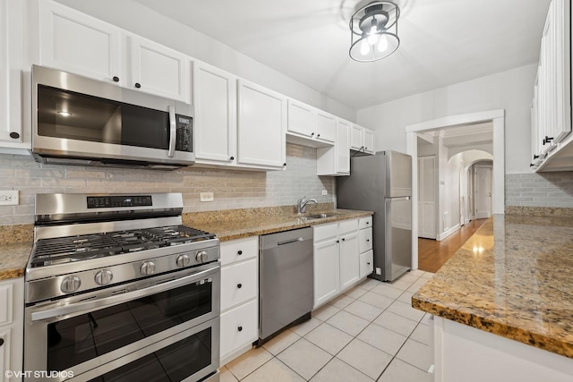 kitchen with arched walkways, white cabinetry, stainless steel appliances, and light stone counters