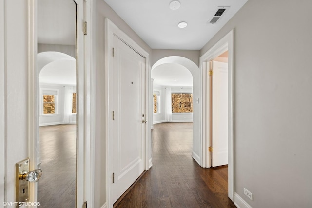 corridor with arched walkways, dark wood-style floors, visible vents, and baseboards