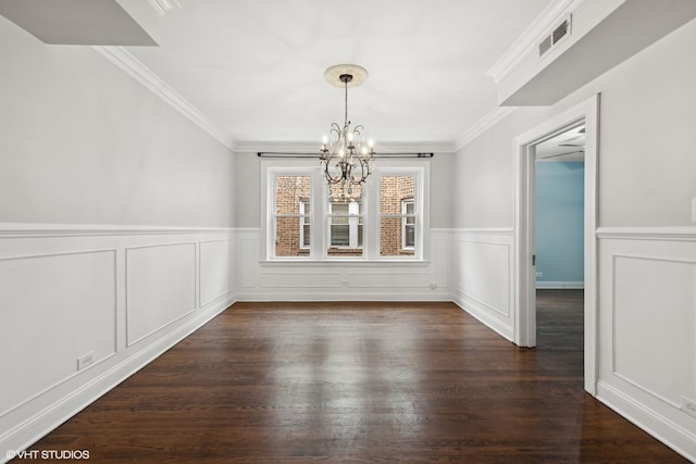 unfurnished dining area with visible vents, ornamental molding, wainscoting, dark wood finished floors, and an inviting chandelier