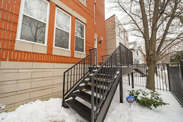 snow covered property entrance with fence and brick siding