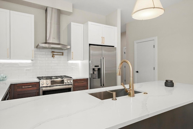 kitchen with backsplash, appliances with stainless steel finishes, white cabinets, a sink, and wall chimney exhaust hood