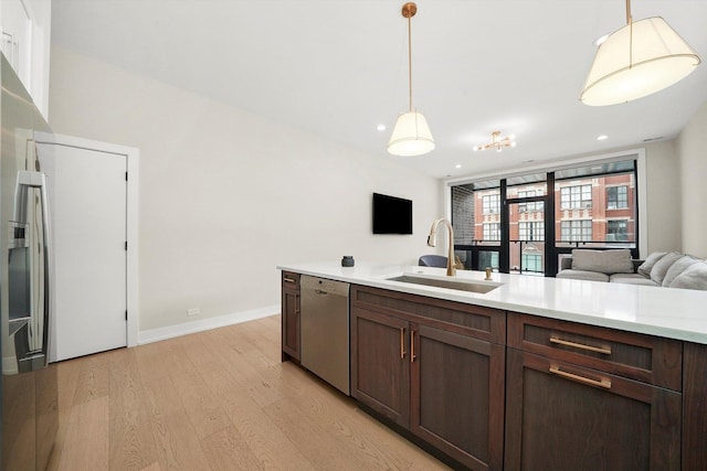 kitchen with dishwasher, hanging light fixtures, light countertops, light wood-type flooring, and a sink