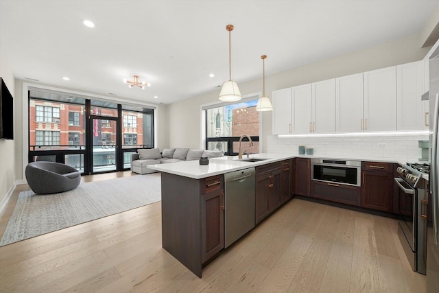 kitchen with stainless steel appliances, a sink, white cabinetry, open floor plan, and decorative backsplash