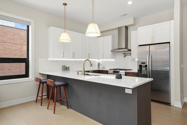 kitchen featuring decorative backsplash, appliances with stainless steel finishes, a sink, wall chimney range hood, and a peninsula