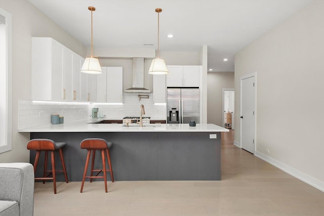 kitchen with a peninsula, a breakfast bar, stainless steel fridge with ice dispenser, wall chimney range hood, and decorative backsplash