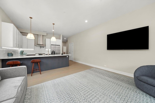 kitchen featuring stainless steel fridge, open floor plan, wall chimney range hood, white cabinetry, and backsplash