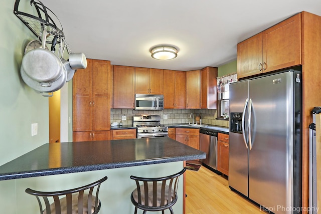 kitchen featuring appliances with stainless steel finishes, sink, backsplash, a breakfast bar, and light wood-type flooring