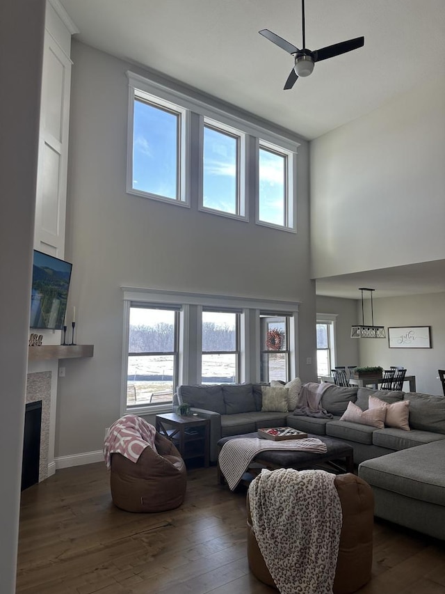 living room with a fireplace, dark wood-type flooring, ceiling fan, and a healthy amount of sunlight