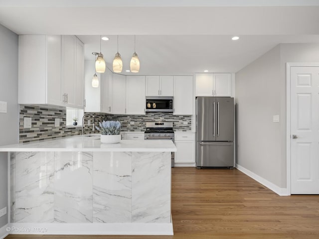 kitchen featuring hanging light fixtures, wood-type flooring, stainless steel appliances, decorative backsplash, and white cabinetry