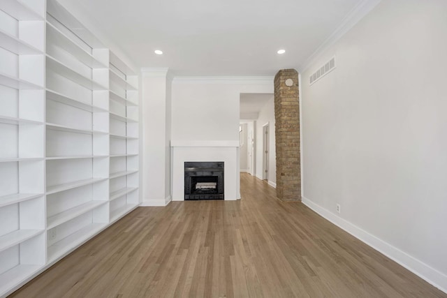 unfurnished living room with baseboards, visible vents, crown molding, light wood-style floors, and a fireplace