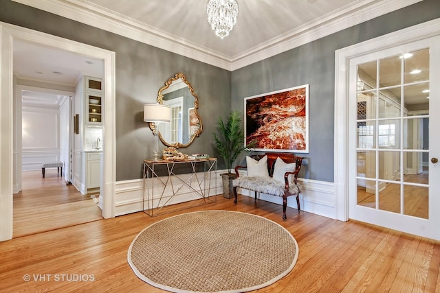 sitting room with a decorative wall, an inviting chandelier, crown molding, and wood finished floors