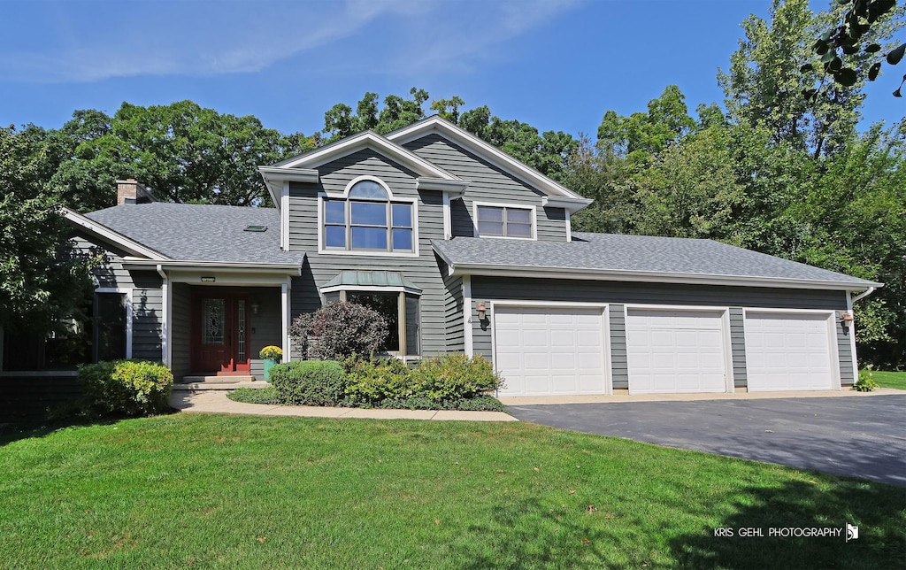 traditional-style home with an attached garage, roof with shingles, driveway, and a front lawn