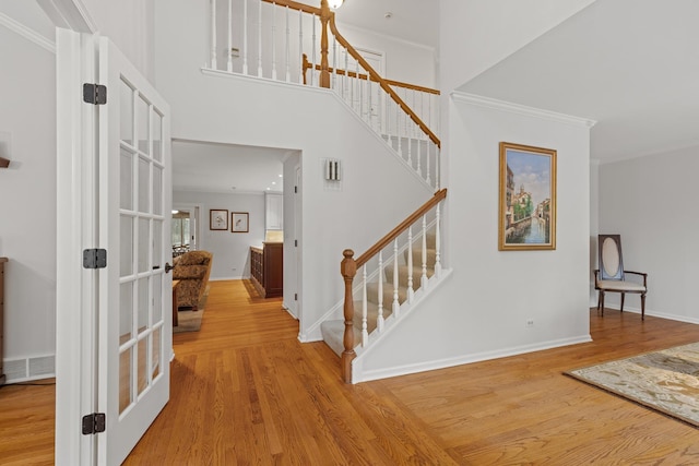 entryway with wood-type flooring, ornamental molding, and a towering ceiling