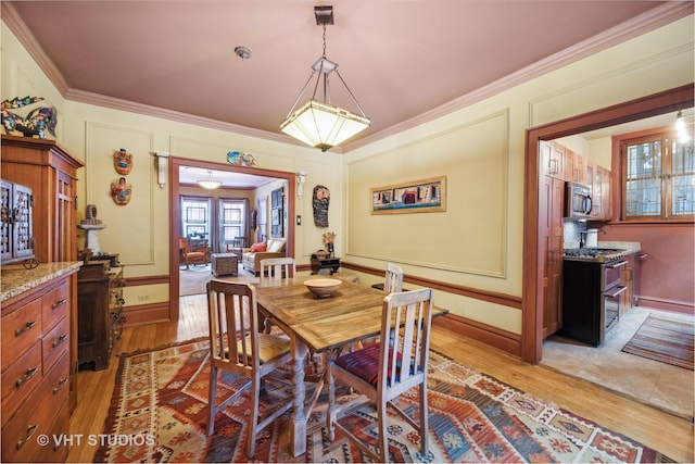 dining space with ornamental molding, baseboards, a decorative wall, and light wood finished floors