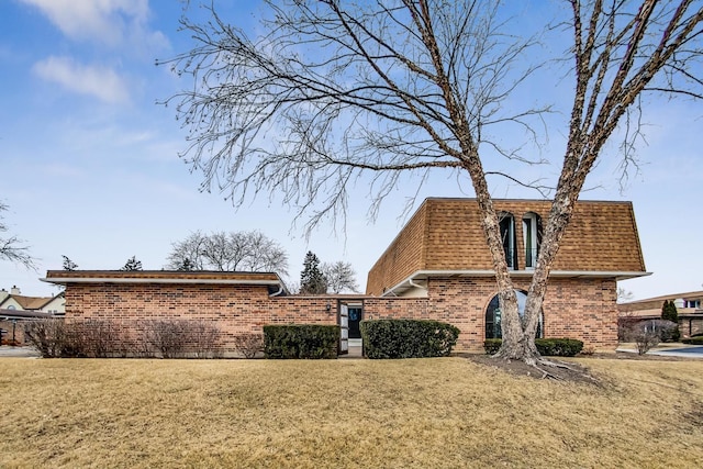 view of home's exterior featuring a yard, mansard roof, roof with shingles, and brick siding